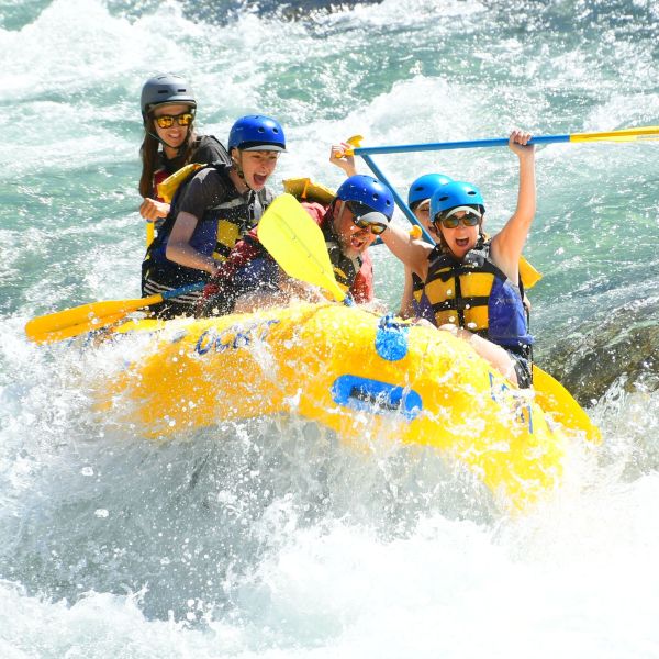 Group of people white-water rafting on a river, all wearing helmets and life vests.