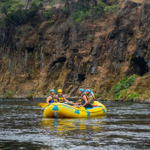 Group rafting on a river near rocky cliff with trees.