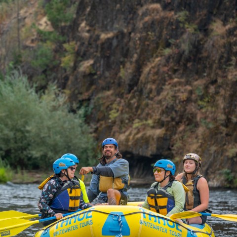 Group rafting on a river with safety gear and helmets.