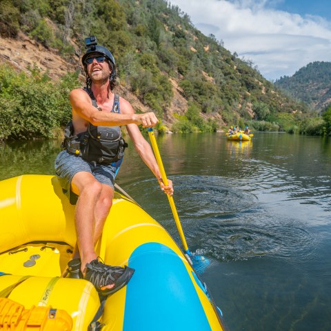 Man rowing a yellow raft on a river, wearing a helmet and life vest.