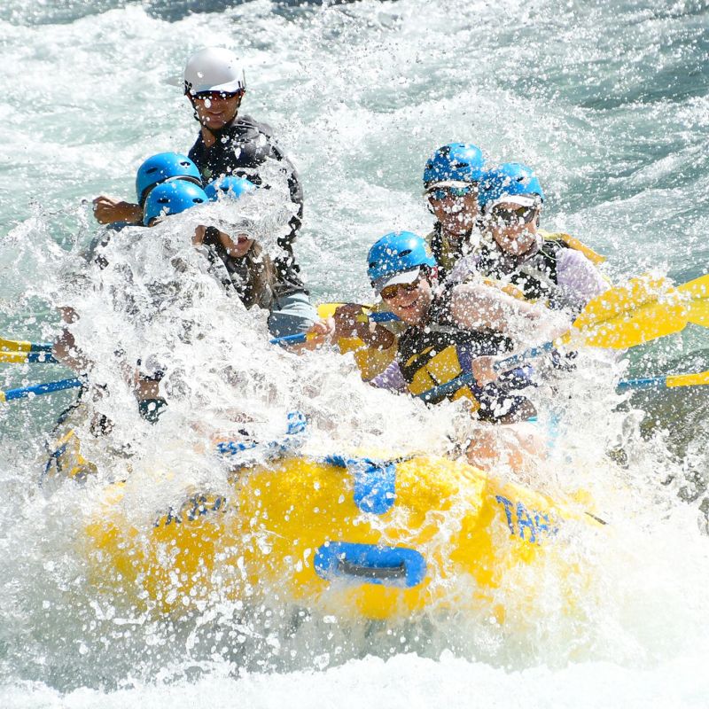 Group of people in helmets rafting on a river with splashing water.