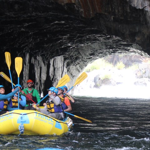 Group rafting through a rocky tunnel on a river.
