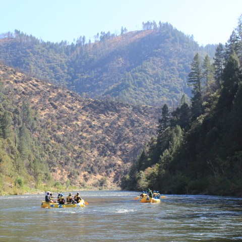 People rafting on a river surrounded by forested hills.