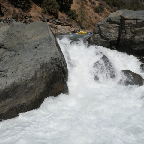 Rafting boat on turbulent river surrounded by large rocks.