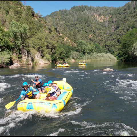 People rafting on a river surrounded by forested hills.