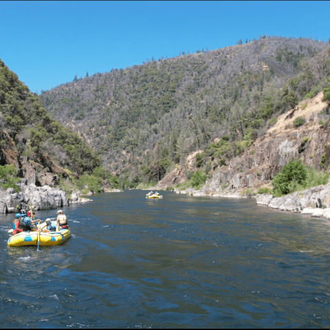 People rafting on a river between tree-covered hills.