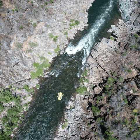 Aerial view of a raft navigating a narrow, rocky river gorge.