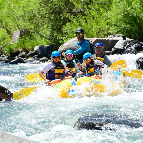 Group rafting on a river, wearing helmets and vests.