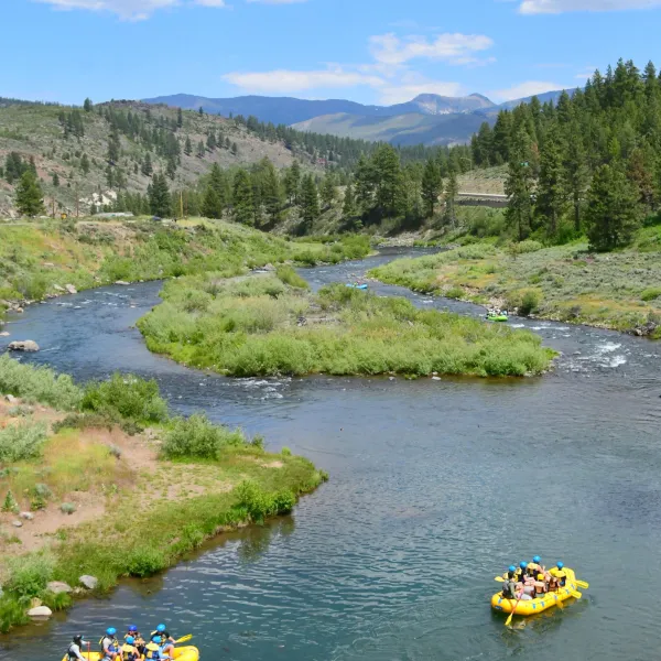 Two yellow rafts on a river surrounded by trees and mountains under a cloudy sky.