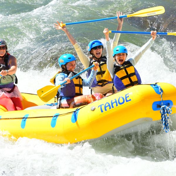 Four people in helmets and vests rafting on Whitewater in a yellow inflatable boat.