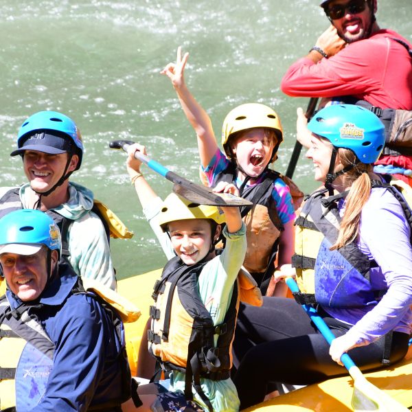 Group of people river rafting, smiling and holding paddles, wearing helmets and life jackets.