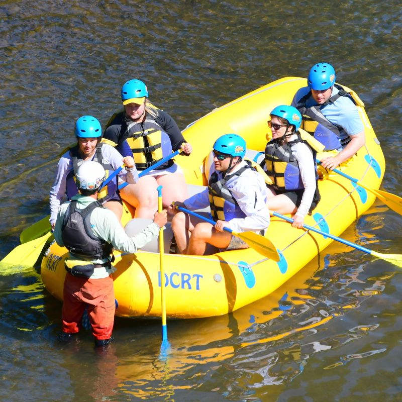 Group in safety gear rafting on a river in a yellow inflatable boat.