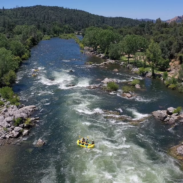 Rafting group on a river with forested banks and hills in the background.