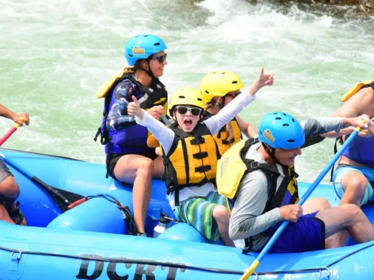 Group in helmets whitewater rafting in a blue inflatable raft.